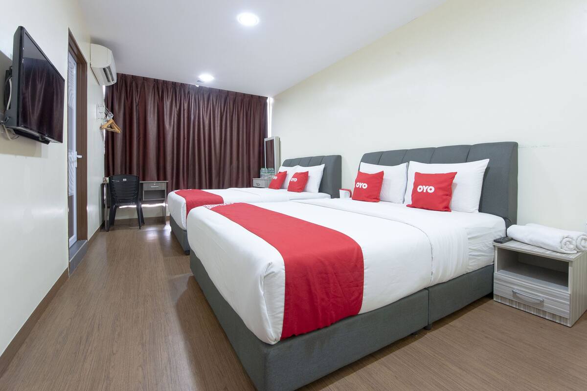 Ein Hotelzimmer mit zwei Betten, einem Fernseher, einer Klimaanlage, einem Schreibtisch und einem Stuhl.