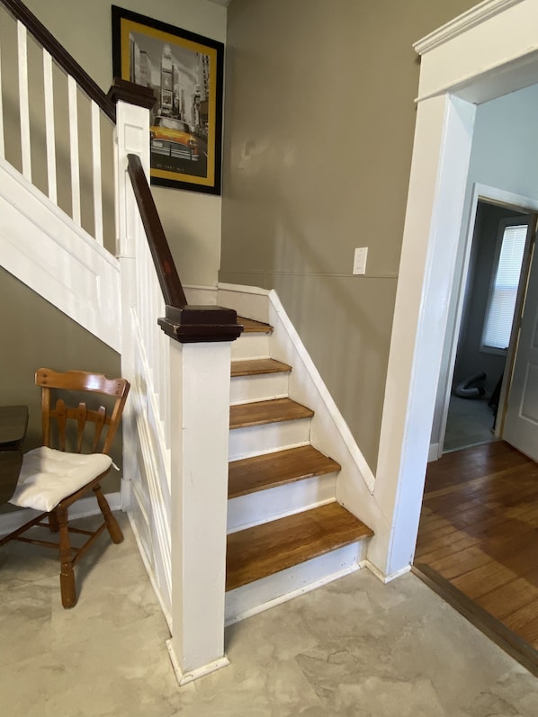 A staircase with wooden steps and white railings, leading to a room with a framed picture on the wall.