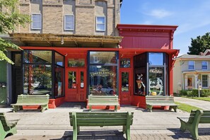 A storefront with a red awning, a bench in front, and a building with a brick facade in the background.