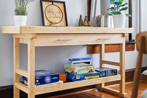 Uma mesa de madeira com uma moldura com uma frase, uma planta em vaso e vários jogos de tabuleiro.