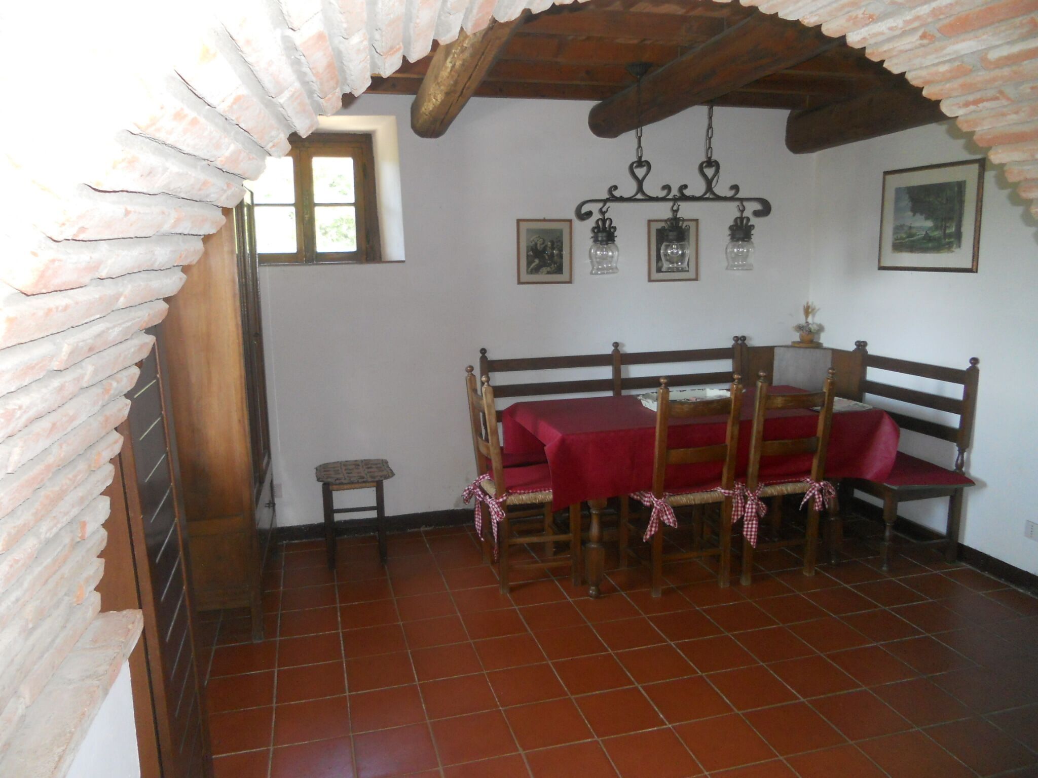 A dining area with a red table and wooden chairs, a small window, and a tiled floor.
