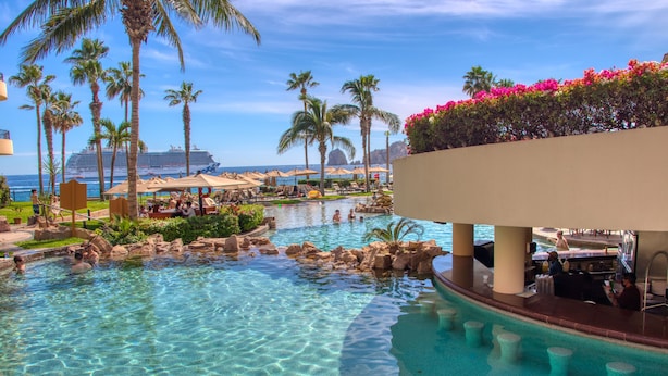Piscina de resort con agua cristalina, palmeras y vista a un crucero al fondo.
