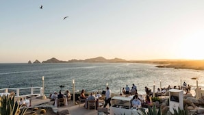 Restaurante frente al mar con terraza al aire libre, con vista a islas distantes y cielo despejado.