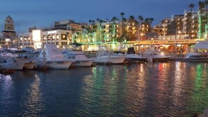 Un puerto deportivo con barcos amarrados, un paseo marítimo y edificios con letreros iluminados.