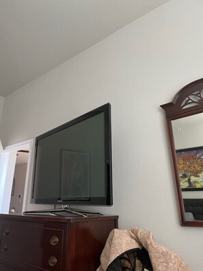 A room with a flat-screen TV mounted on a dresser, a wooden cabinet, and a framed mirror on the wall.