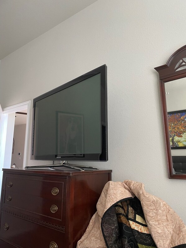 A room with a flat-screen TV mounted on a wooden dresser, a mirror on the wall, and a door leading to another room.