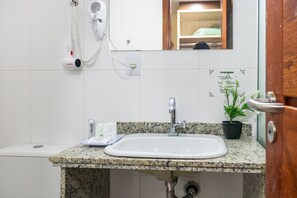 A bathroom with a granite countertop sink, a handheld hair dryer mounted on the wall, a small potted plant, and a mirror above the sink.