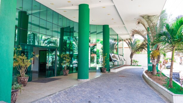 Un edificio moderno con fachada de vidrio, pilares verdes y plantas en macetas.