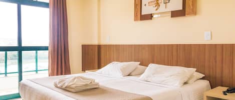 Habitación de hotel con una cama grande, cabecera de madera, aire acondicionado de pared, una obra de arte enmarcada y una mesita de noche con un teléfono.