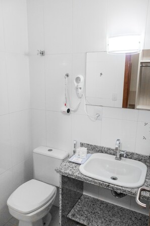 A small, clean bathroom with a white toilet, a sink with a mirror above it, and a hairdryer on the wall.