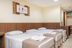 A hotel room with four beds arranged in a row, a wooden headboard, a wall-mounted artwork, and a small table with a towel.