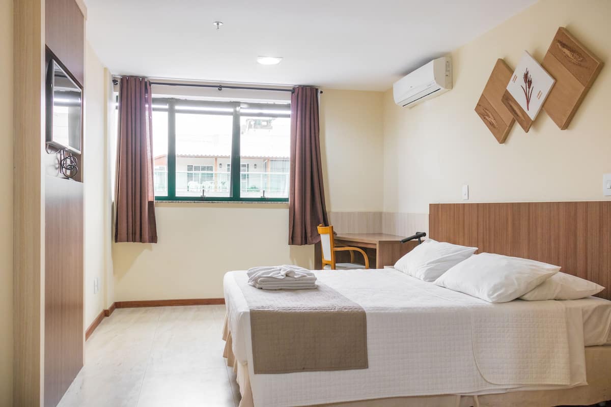 Una habitación de hotel con cama, escritorio, silla y ventana con cortinas.