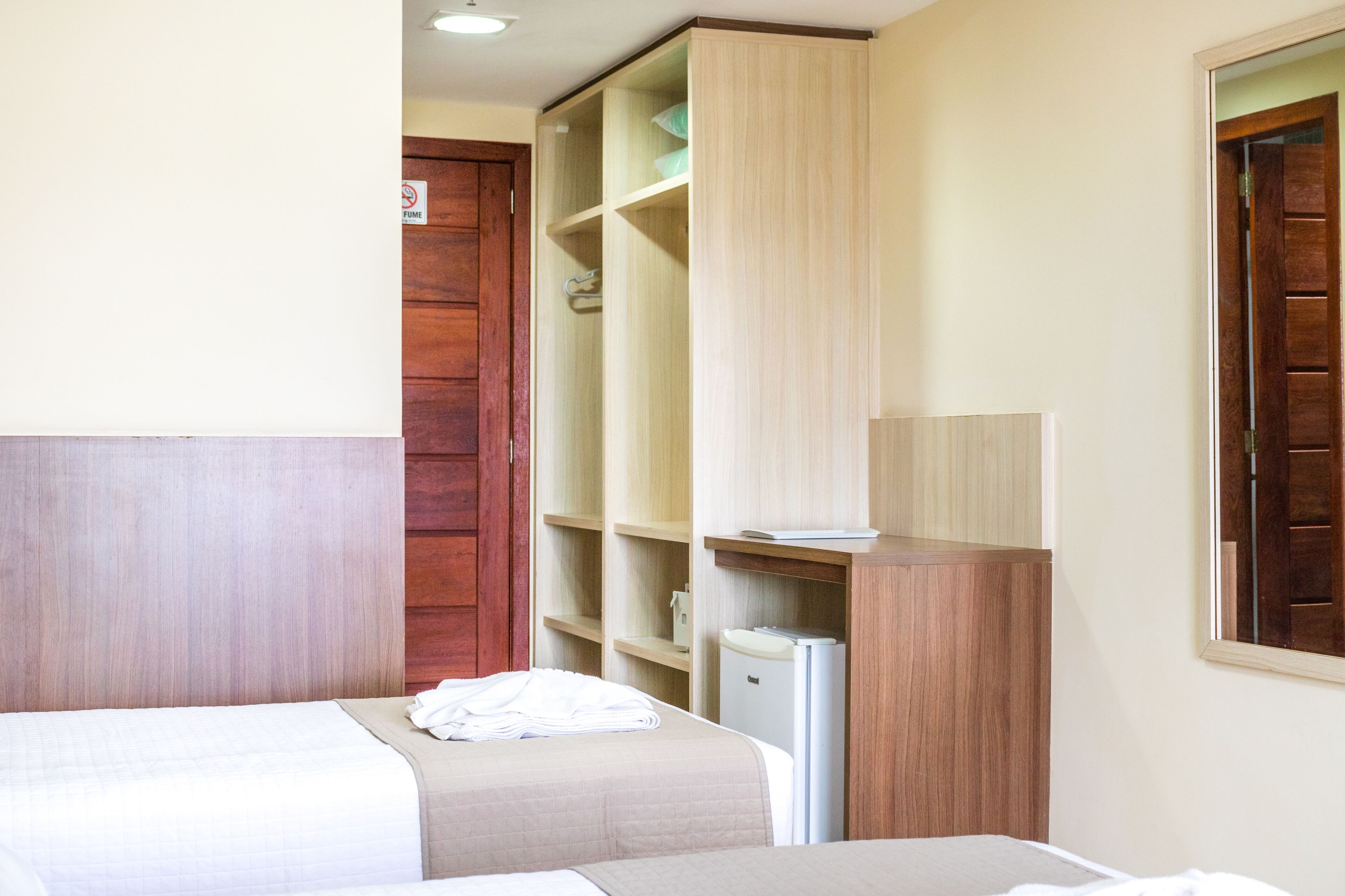 A hotel room with a bed, a wardrobe, a desk, and a small refrigerator.