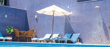 Uma área de piscina com paredes azulejadas em azul, espreguiçadeiras e uma mesa com cadeiras.