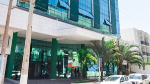 Un hotel moderno con fachada de vidrio, entrada cubierta y una palmera frente a él.
