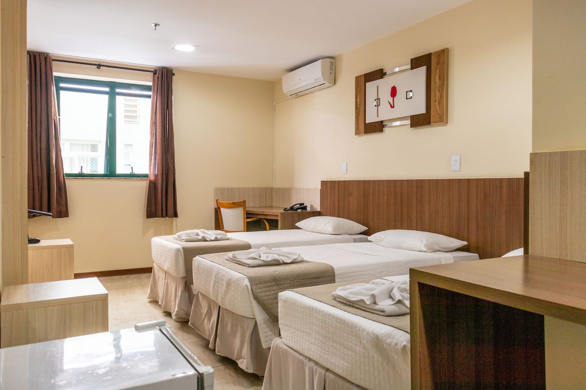 Una habitación de hotel con dos camas, un escritorio, una silla y una ventana con cortinas.