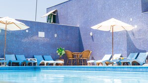 Un área de piscina con sillones de descanso y sombrillas, un muro de azulejos y una pequeña mesa con sillas.