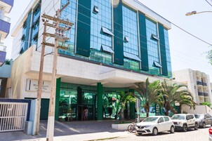 Un hotel moderno con fachada de vidrio, entrada cubierta y un estacionamiento con varios automóviles.