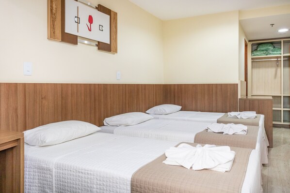 A hotel room with three beds, wooden headboard, a wall-mounted artwork, and a closet with green towels.