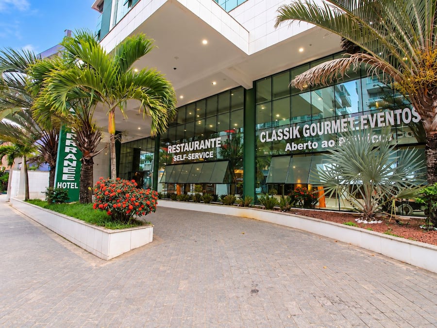 Entrada de un hotel con fachada de vidrio moderna, un letrero de restaurante y una palmera.