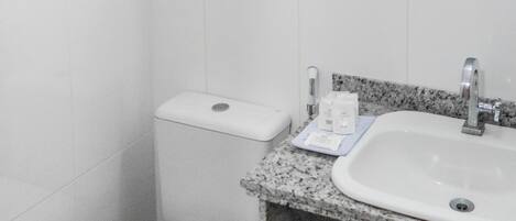 A bathroom with a toilet, a sink, a mirror, and a hairdryer mounted on the wall.