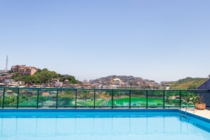 Ein Schwimmbecken mit Blick auf eine Stadtlandschaft und Grün im Hintergrund.