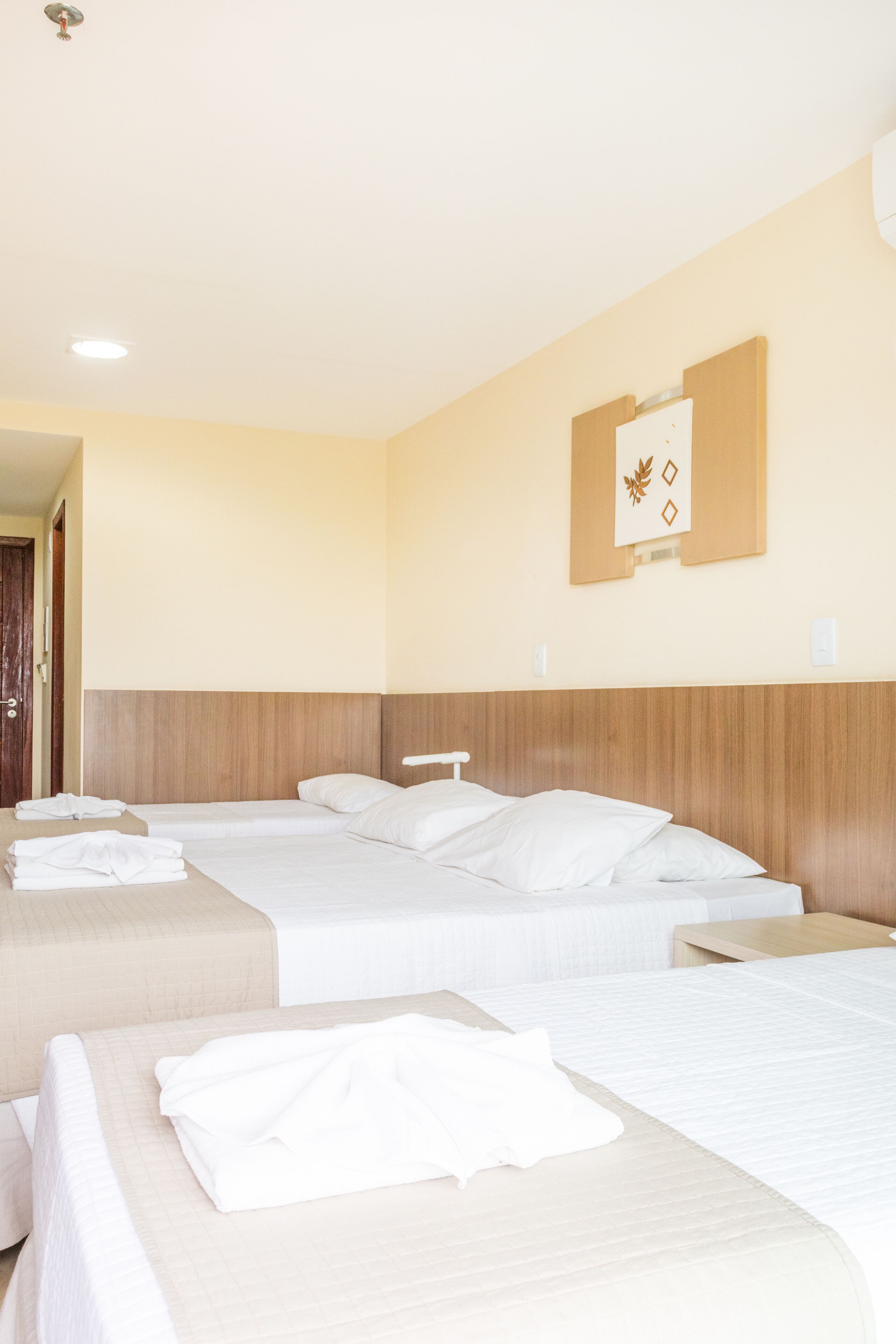 A hotel room with three beds, a wooden headboard, and a wall-mounted artwork.