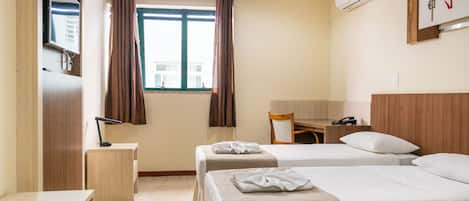 A hotel room with two beds, a desk, a chair, a TV, and an air conditioning unit.