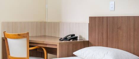 Une chambre d’hôtel avec un bureau en bois, une chaise, un lit avec un oreiller blanc et un téléphone sur le bureau.