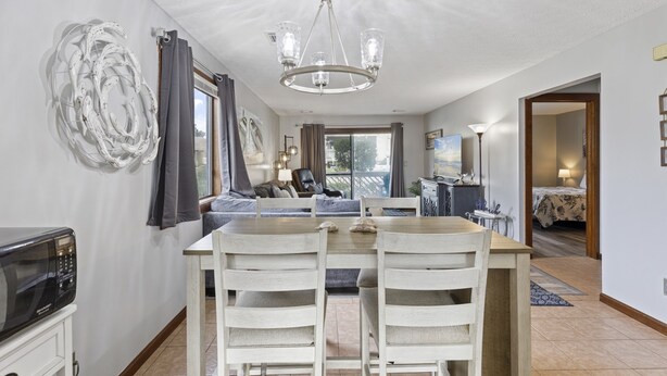 Un comedor con una mesa de madera y sillas blancas, un candelabro y vistas al exterior a través de una ventana.