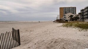 Una playa con una valla de madera, un edificio de varios pisos y un cielo despejado.