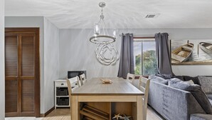 Comedor con mesa y sillas de madera, una araña y vista a los barcos a través de una ventana.
