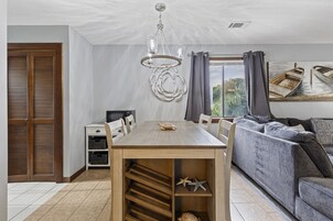 Comedor con mesa y sillas de madera, una araña y vista a los barcos a través de una ventana.
