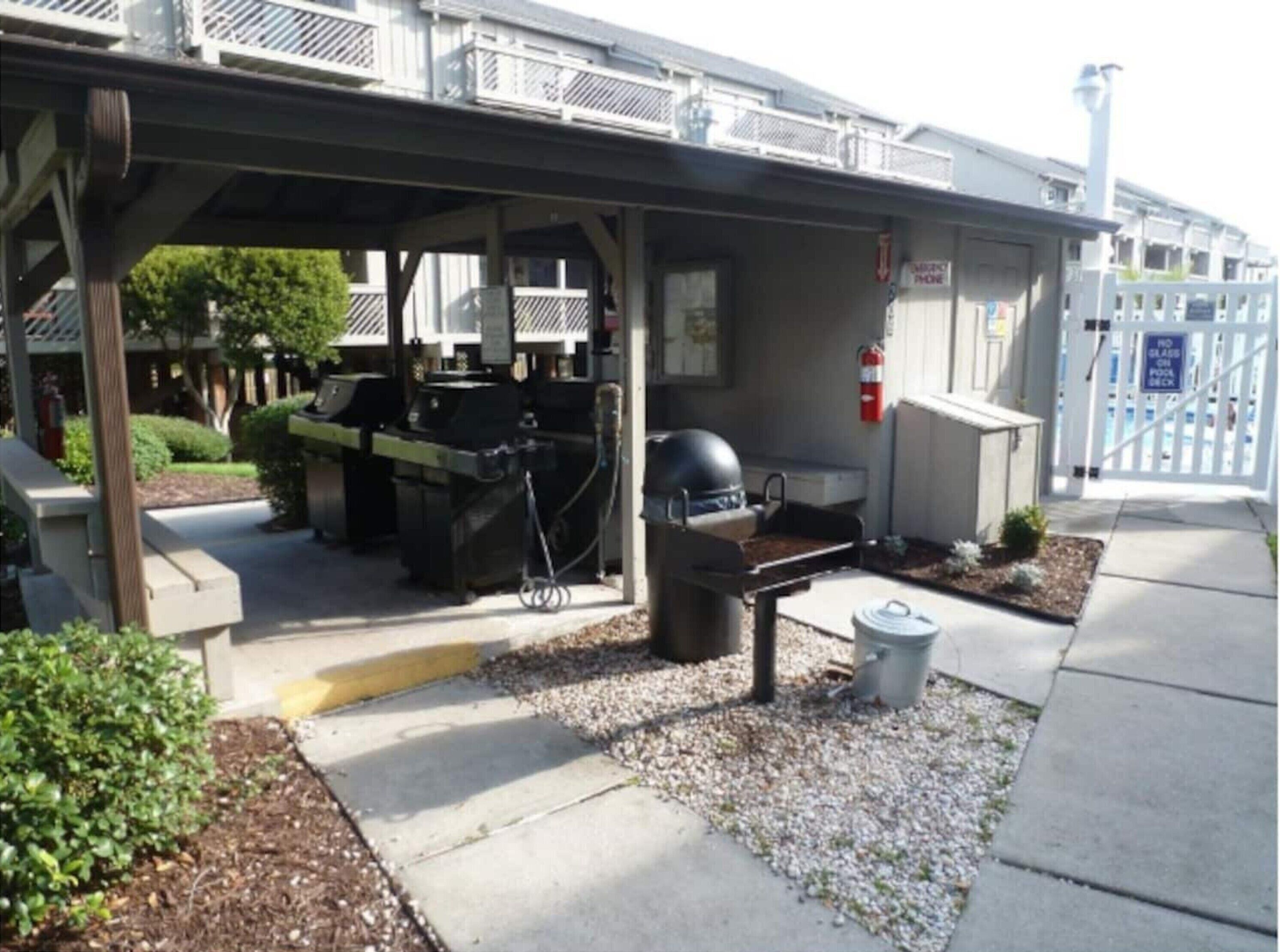 An outdoor barbecue area with a grill and a trash bin, under a covered structure.