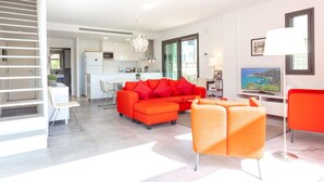 Una sala de estar moderna con un sofá naranja brillante, un sillón a juego y una zona de comedor con una mesa y sillas blancas.