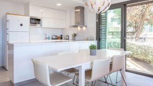 Una cocina moderna con armarios blancos, horno empotrado y un comedor con mesa y sillas blancas.