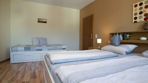 Une chambre d’hôtel avec deux lits, un plancher en bois, un mur avec une étagère et un luminaire au plafond.