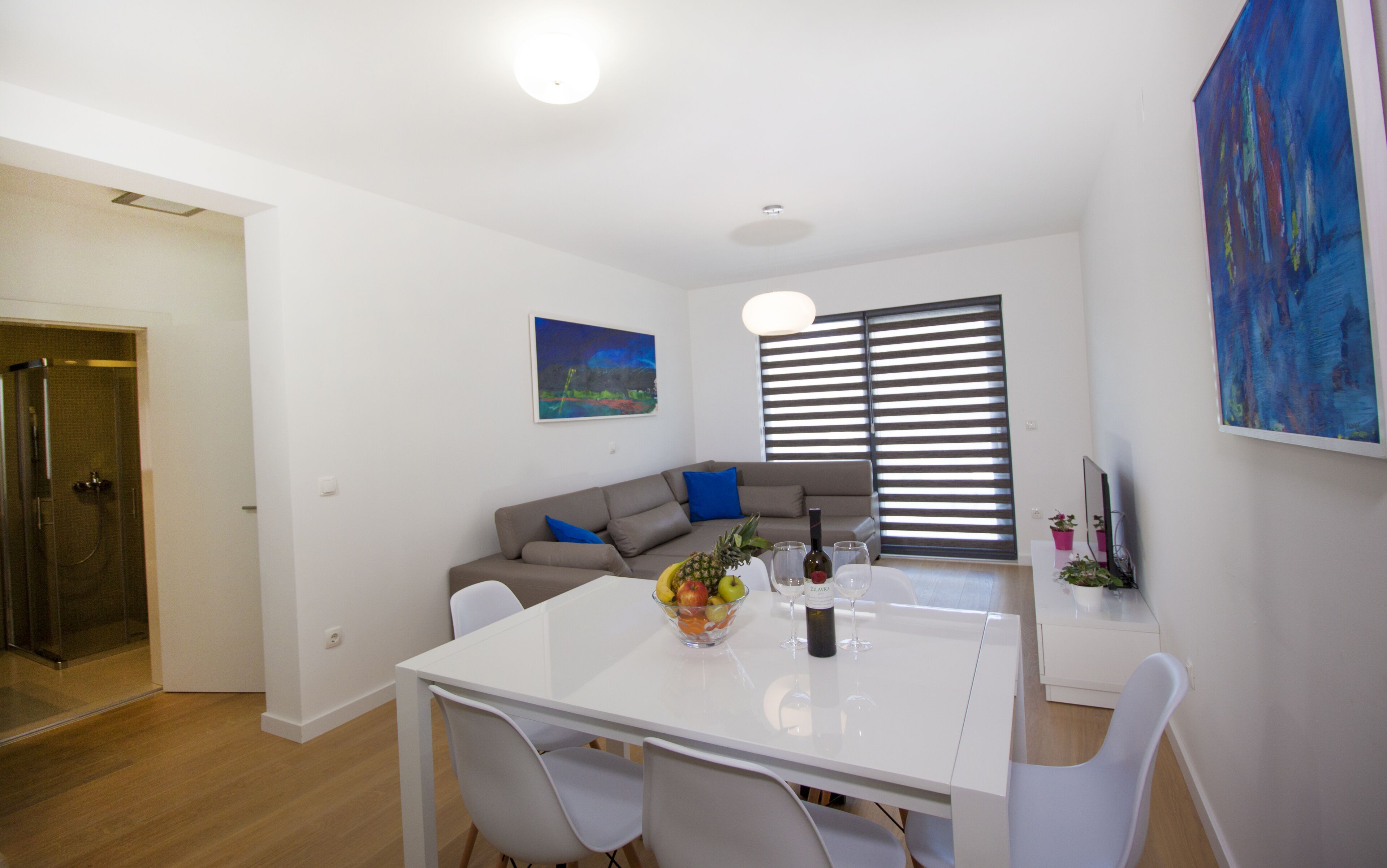 Una sala de estar moderna con un sofá blanco, una mesa de comedor con sillas, un frutero y un cuadro en la pared.