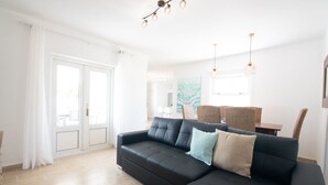 A modern living room with a black sectional sofa, a dining table with chairs, and a large window with curtains. - Newly renovated penthouse in a complex with pool on the seafront (Costa Teguise)