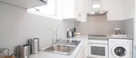 A modern kitchen with a stainless steel sink, a built-in oven, and a front-loading washing machine.