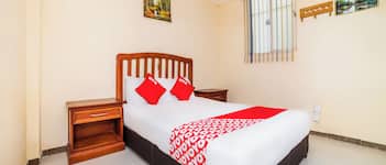 Un dormitorio ordenado con cama de madera, una mesita de noche y un ventanal con barrotes.
