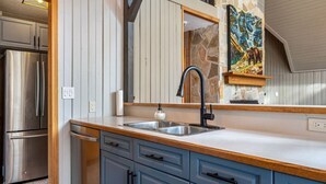 A kitchen with a stainless steel refrigerator, a double sink, and blue cabinets. - The Legacy Cabin | Hot Tub | Huge Fenced Yard (Windermere)