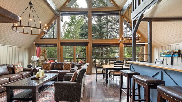 A spacious living area with a large window, a wooden ceiling, and a bar area. - The Legacy Cabin | Hot Tub | Huge Fenced Yard (Windermere)