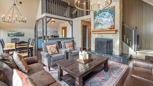 A spacious living area with a fireplace, a dining area, and a staircase leading to an upper level. - The Legacy Cabin | Hot Tub | Huge Fenced Yard (Windermere)
