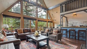 A spacious living area with a large window, a wooden ceiling, and a bar area. - The Legacy Cabin | Hot Tub | Huge Fenced Yard (Windermere)