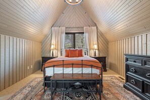 A bedroom with a sloped ceiling, a bed with an orange and white bedspread, a wooden dresser, and a patterned rug.