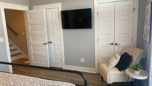 Une chambre à coucher comprenant un lit, une chaise, une petite table avec une plante et un téléviseur fixé au mur.