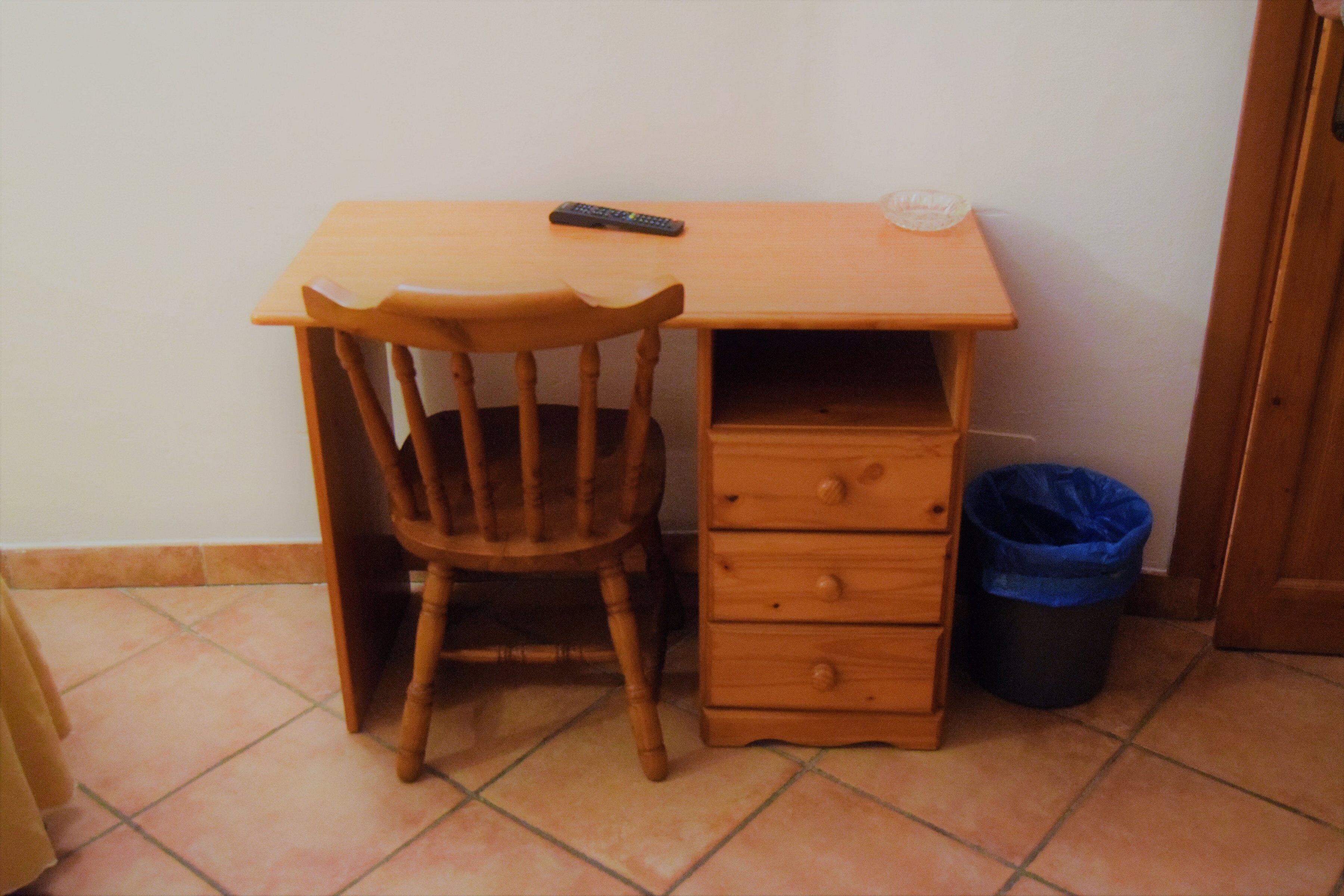 A small wooden desk with a chair, a drawer, and a trash bin.