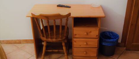 A small wooden desk with a chair, a drawer, and a trash bin.