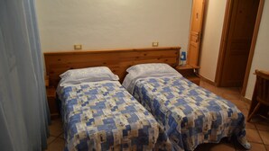 Une chambre avec deux lits simples, des têtes de lit en bois, une porte en bois et un sol carrelé.